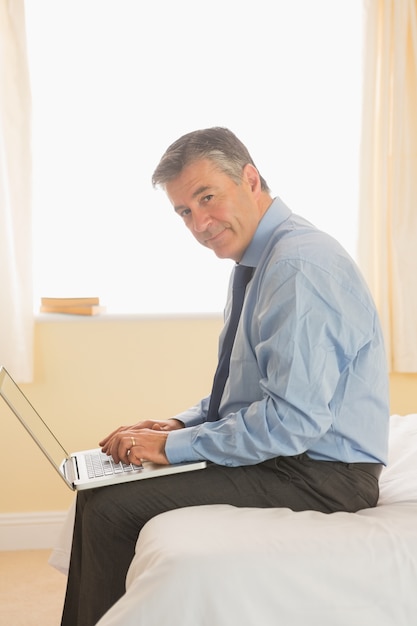 Skupiający się mężczyzna używa laptopu obsiadanie na łóżku