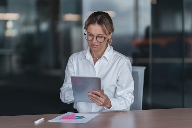 Skupiona bizneswoman w okularach pracuje na cyfrowym tablecie w swoim miejscu pracy w biurze