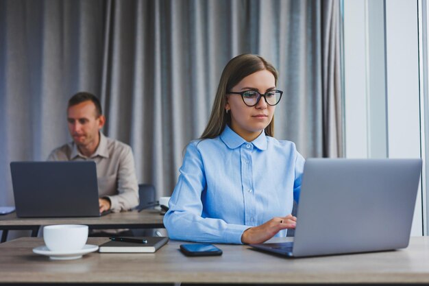 Skupiona kobieta w codziennych ubraniach, pisząca na netbooku podczas pracy nad nowym projektem, siedząc przy biurku w nowoczesnym miejscu pracy Biznesowa dama w kurtce i okularach Praca zdalna
