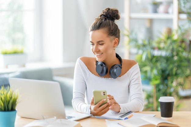 Skupiona młoda bizneswoman studiuje online, ogląda webinarium, podcast na laptopie, robi notatki, siedzi przy biurku. Koncepcja e-learningu.