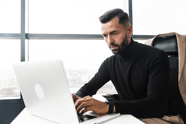 Skupiony biznesmen pracuje na laptopie siedząc w biurze