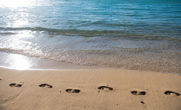 Ślady na złotym piasku ślady na plaży w tle spokojna piękna fala oceanu na piaszczystej plaży wi...