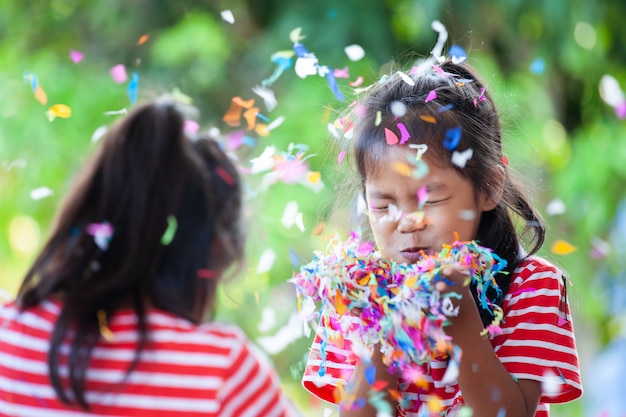 Śliczna azjatykcia dziecko dziewczyna i jej siostra bawić się z kolorowymi confetti wpólnie świętować w przyjęciu