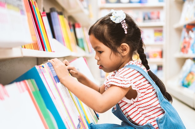 Śliczna azjatykcia dziecko dziewczyny wybiórki książka na półka na książki w bookstore w supermarkecie