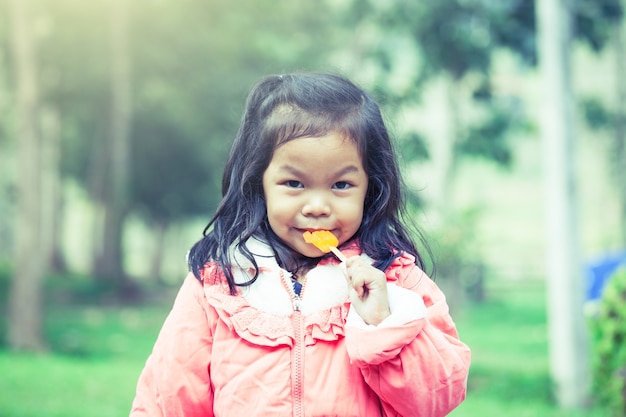 Śliczna azjatykcia mała dziewczynka je lody w parku w rocznika koloru filtrze