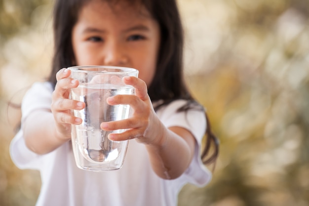 Śliczna azjatykcia mała dziewczynka trzyma szkło świeża woda w rocznika koloru brzmieniu