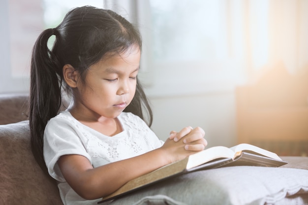 Śliczna azjatykcia małe dziecko dziewczyna zamykał ona oczy i składał jej rękę w modlitwie na Świętej biblii