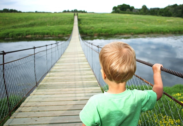 Zdjęcie Śliczna berbeć chłopiec na zawieszenie moscie przez rzekę. podróż przygodowa, spójrz w przyszłość, otwierając nową koncepcję drogi