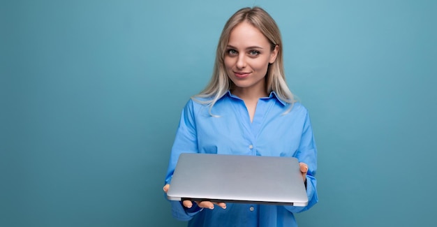 Śliczna blond dziewczyna studentka z laptopem na jaskrawym błękitnym tle