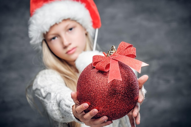 Śliczna Blondynka W Kapeluszu świętego Mikołaja Trzyma Czerwoną Bombkę.