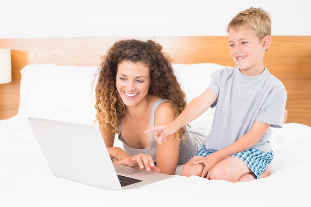 Śliczna blondynki chłopiec i matka na łóżkowym używa laptopie