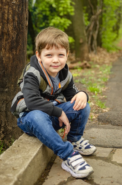 Zdjęcie Śliczna chłopiec cztery lata chodzenia w parku wczesną wiosną. dziecko usiadło, by odpocząć po długim fascynującym spacerze.