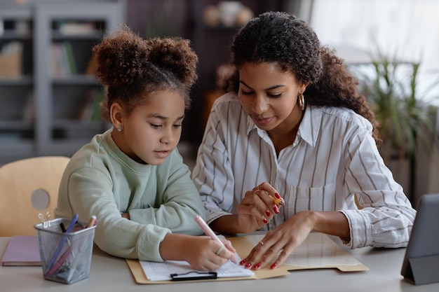 Śliczna czarna dziewczyna robi pracie domowej z matką lub korepetytorem pomaga