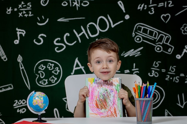 Śliczna Dziecko Chłopiec Robi Pracie Domowej. Sprytne Dziecko Rysunek Przy Biurku. Uczeń. Uczeń Szkoły Podstawowej Rysunek W Miejscu Pracy. Dzieciak Lubi Się Uczyć. Edukacja Domowa. Powrót Do Szkoły. Mały Chłopiec Na Lekcji W Szkole