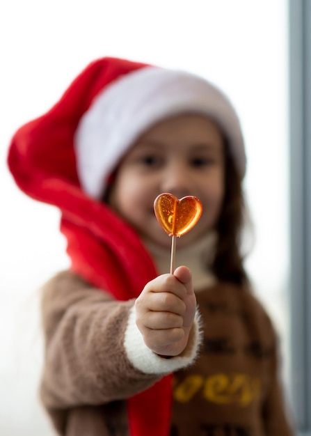Śliczna dziewczyna w czapce Mikołaja trzyma w dłoniach cukierki w kształcie serca Nowy Rok Boże Narodzenie