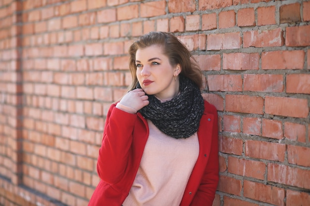 Śliczna dziewczyna w czerwonym płaszczu na tle ściany z cegły