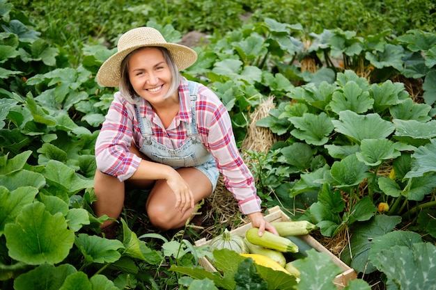 Śliczna dziewczyna w kapeluszu zbieranie najświeższej dyni i cukinii w ogrodzie. Jesienne zbiory warzyw.