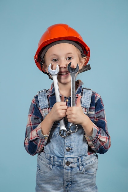 Zdjęcie Śliczna dziewczyna w pomarańczowym kasku pozuje śmiesznie na niebieskim tle, trzymając klucze w obu rękach. koncepcja budowy i naprawy.