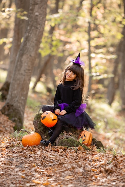 śliczna dziewczyna w stroju wiedźmy siedzi na pniu w jesiennym lesie halloween