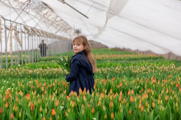 Śliczna dziewczyna z tulipanami o blond włosach wiosną w szklarni z rosnącymi tulipanami