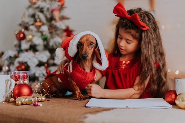 Śliczna dziewczynka i jamnik karłowaty w stroju Świętego Mikołaja świętują Boże Narodzenie i Nowy Rok