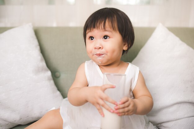 Śliczna dziewczynka pije mleko z mlecznymi wąsami w domu
