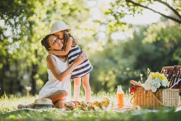 Śliczna dziewczynka przytula i całuje swoją piękną mamę podczas pikniku na łonie natury.