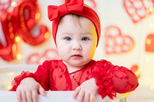 śliczna dziewczynka siedzi w czerwonym body na tle czerwonych serc i napisu love. pojęcie walentynki, walentynki
