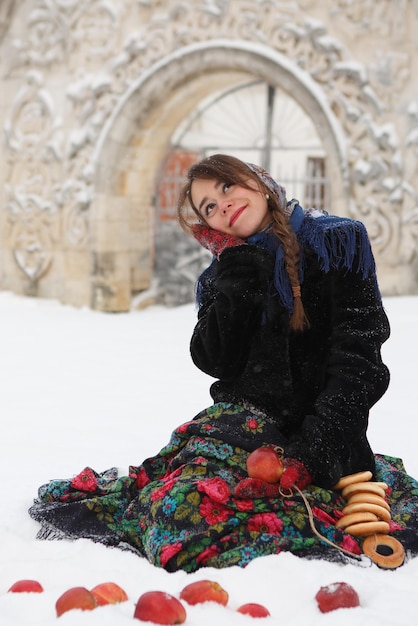 Śliczna kaukaska dziewczyna siedzi na śniegu z bajglami i czerwonymi jabłkami