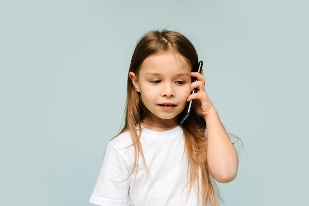 Śliczna Kaukaska Dziewczynka Rozmawia Przez Telefon Na Białym Tle W Studio Na Niebieskim Tle Mała Dziewczynka Słucha Wiadomości Od Mamy