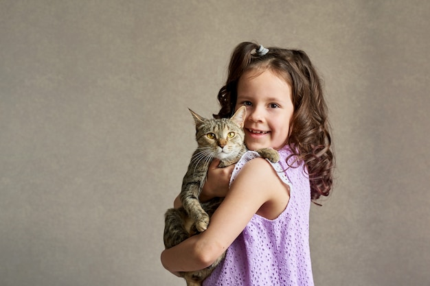 Śliczna kędzierzawa dziewczyna z kotem w jej rękach na szarym tle