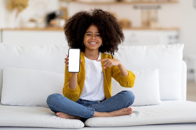 Śliczna ładna mała czarna dziewczyna pokazująca smartfon z pustym ekranem