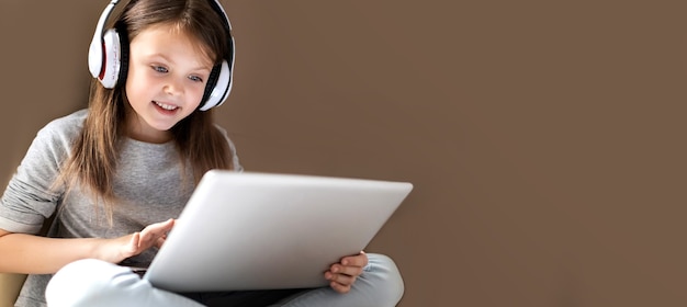 Śliczna mądra dziewczynka w bezprzewodowych słuchawkach za pomocą laptopa w domu
