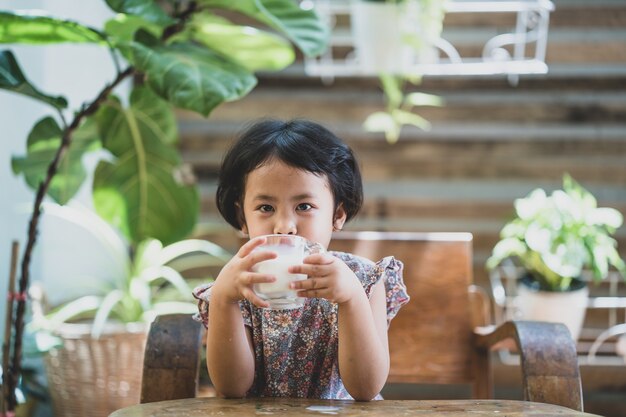 Śliczna mała Azjatycka dziewczyna pijąca świeże organiczne mleko w ogrodzie