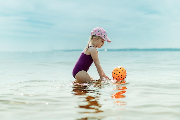 Śliczna mała dziewczynka bawi się gumową piłką w morzu