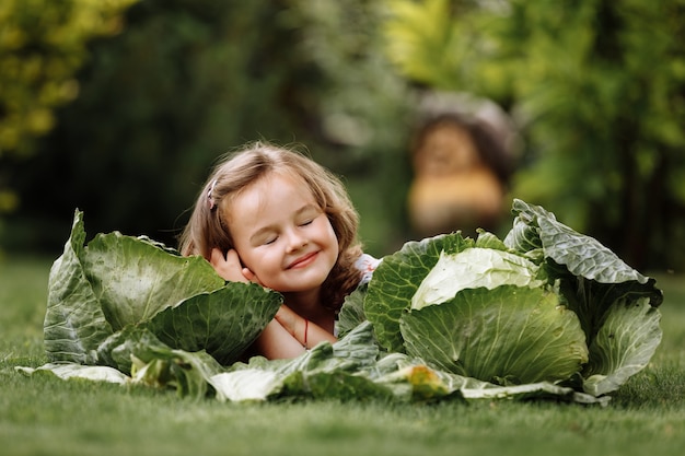 Śliczna mała dziewczynka dobrze się bawi i leży na zielonej trawie w pobliżu kapusty