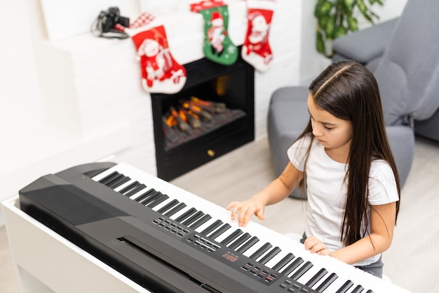 Śliczna mała dziewczynka gra świąteczną melodię na pianinie, wesołych świąt Bożego Narodzenia, szczęśliwych świąt sezonowych