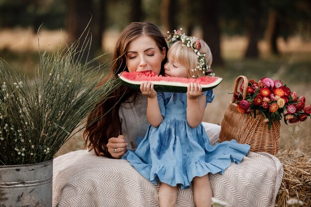 Śliczna mała dziewczynka i jej młoda matka jemy świeżego arbuza w parku