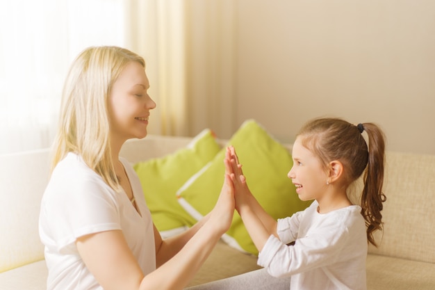 Śliczna mała dziewczynka i jej piękna mama bawią się w domu, klaszcząc w dłonie.