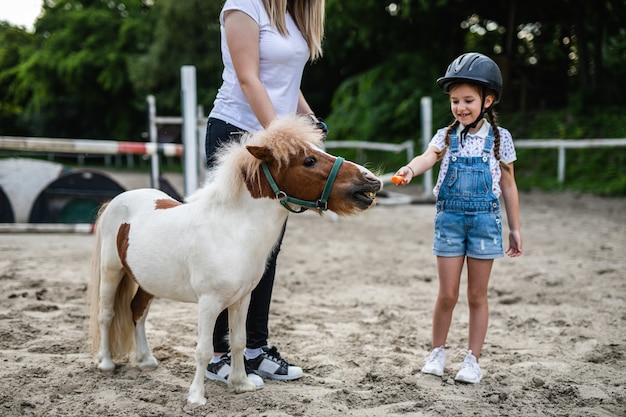 Śliczna mała dziewczynka i jej starsza siostra bawią się z kucykiem na świeżym powietrzu na ranczo.