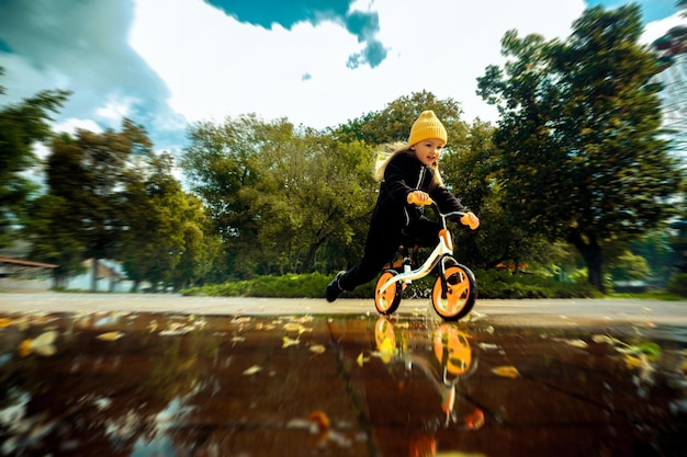 Zdjęcie Śliczna mała dziewczynka jeździ przez kałuże na rowerze w parku
