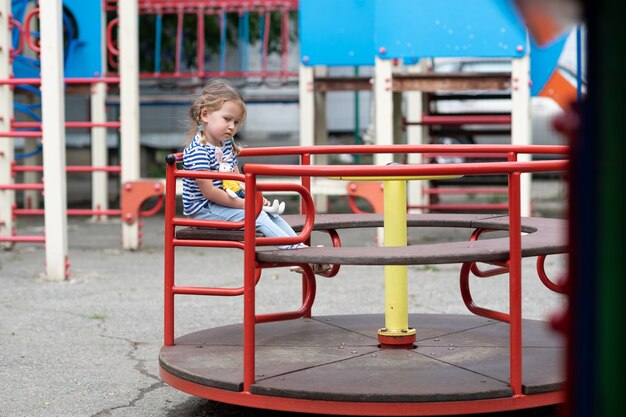 Śliczna mała dziewczynka kręci się samotnie na czerwonej karuzeli na opuszczonym placu zabaw