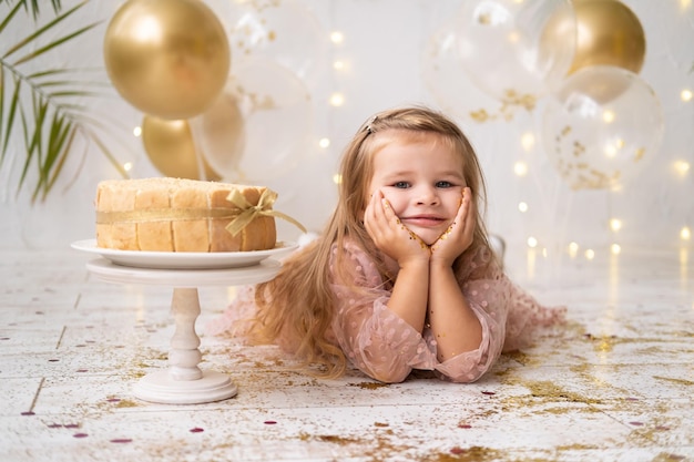 Śliczna mała dziewczynka leżąca na podłodze w pobliżu tortu urodzinowego uśmiechnięta świętująca urodziny