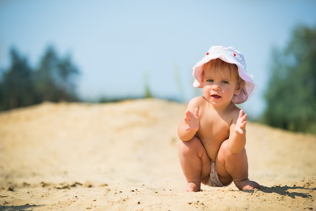 Śliczna mała dziewczynka macha cześć siedząc na piasku