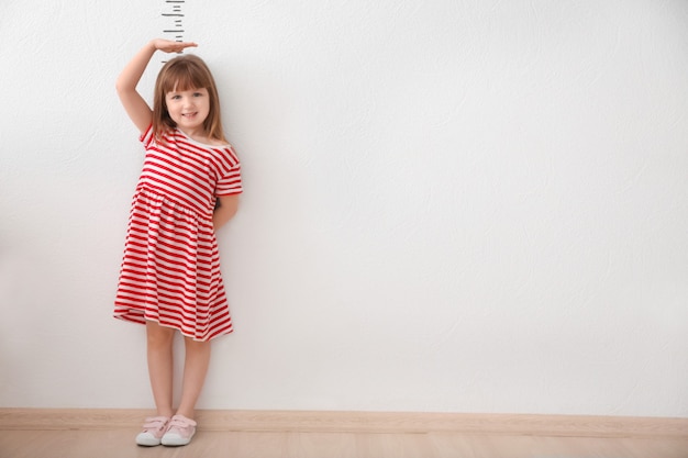 Śliczna mała dziewczynka mierzy wysokość w pobliżu jasnej ściany