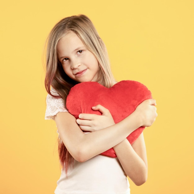 Śliczna mała dziewczynka mocno przytula duże czerwone zabawkowe serce