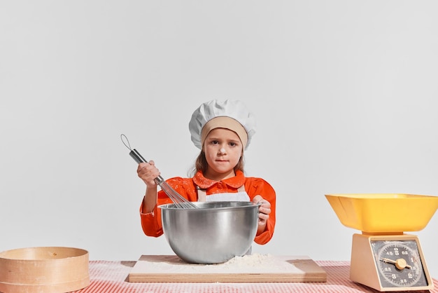 Śliczna mała dziewczynka na obrazku szefa kuchni gotującego na szarym tle mieszania ciasta