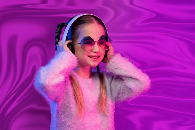 Śliczna mała dziewczynka nosi okulary przy użyciu słuchawek na abstrakcyjnym tle