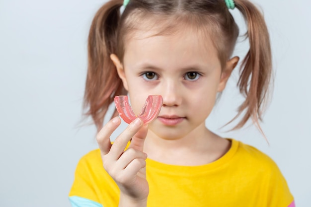 Śliczna mała dziewczynka o blond włosach trzyma różowego dentystycznego trenera myofunkcjonalnego