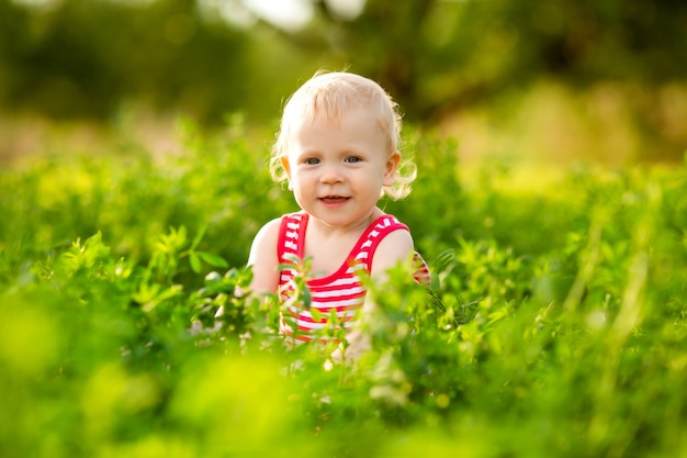 Śliczna mała dziewczynka ono uśmiecha się w czerwonym lato sukni odprowadzeniu na zielonym gazonie